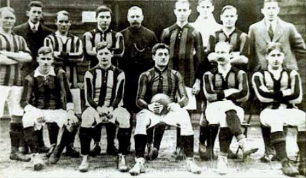 Ein Schwarz-Weiß-Foto einer Fußballmannschaft, wobei einige Spieler stehen und einige sitzen, vor einer Wand, mit dem Text "Ballymena Football Club" unten.