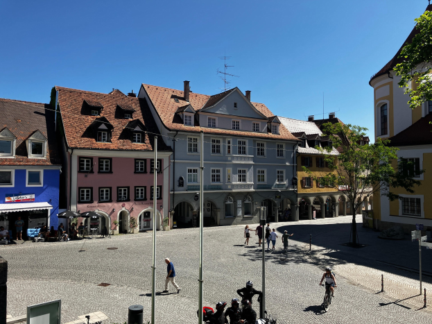 Eine Gruppe von Menschen, die auf Fahrrädern eine Kopfsteinpflasterstraße in der Altstadt von Heidelberg entlangfahren, mit Gebäuden, Laternenpfählen, Bäumen, Bänken und einem sichtbaren Himmel im Hintergrund.