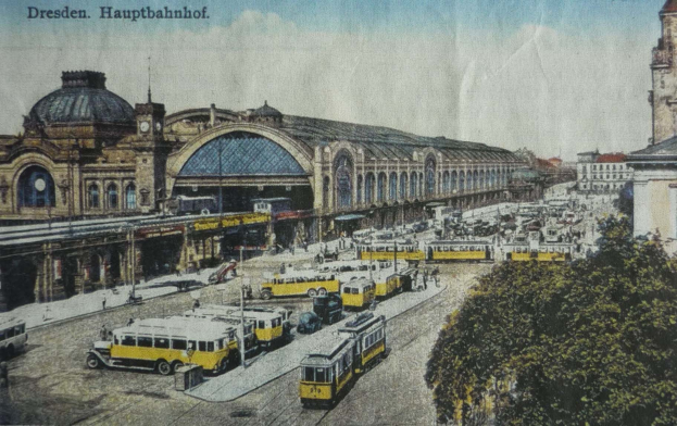 Schwarze und weiße Postkarte des Dresdner Hauptbahnhof Bahnhofs in Dresden, Deutschland, zeigt eine belebte Straßenszene mit Fahrzeugen, Fußgängern, Bäumen, Gebäuden und einem bewölkten Himmel.