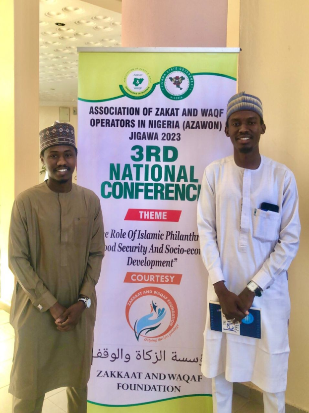 Zwei Männer stehen nebeneinander vor einem Banner mit der Aufschrift "3. Nationalkonferenz" mit einer Säule und Deckenbeleuchtung im Hintergrund.
