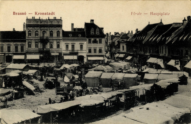 Altes Schwarz-Weiß-Foto eines belebten Marktes in Kronstadt, Deutschland, mit Menschen, Zelten und Gebäuden im Hintergrund unter einem sichtbaren Himmel.