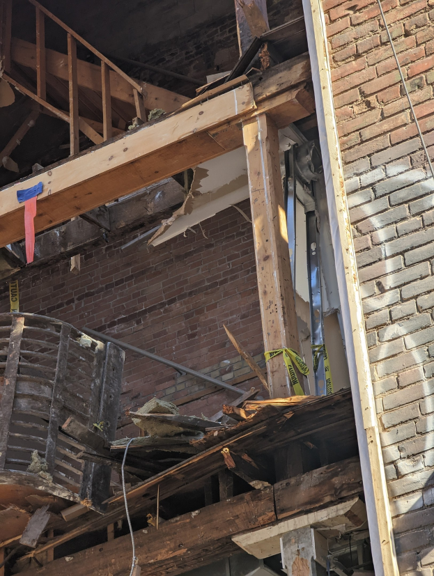 Ein teilweise abgerissenes Gebäude mit verstreuten Holzplanken und Trümmern, zerbrochene Fenster und Türen.
