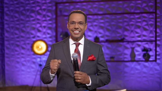 Stephen Colbert, Moderator von 'The Daily Show with Trevor Noah', steht auf einer Bühne und hält ein Mikrofon in der Hand, trägt einen Anzug, eine Krawatte und eine Brille, mit einem Scheinwerfer und einem Ständer hinter ihm.