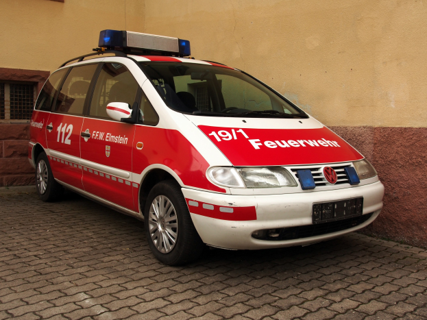 Ein roter und weißer Minivan mit Notarztkennzeichen vor einem Fensterbau geparkt.