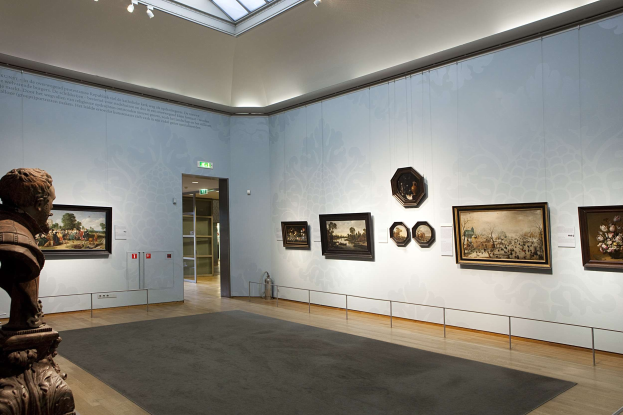 Ein prächtiger Museumsraum mit einer Statue links, Teppichboden, Fotorahmen an den Wänden, einer Glaskuppel mit Lichtern und Türen im Hintergrund.