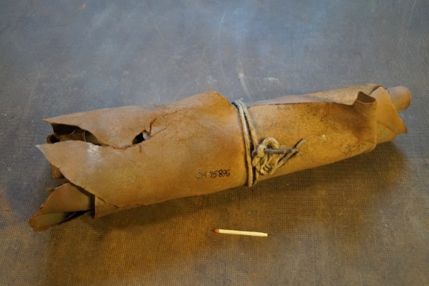 Eine braune Papiertüte, die wie eine Granate aussieht, mit einem Seil verschnürt und auf einen Tisch gelegt, mit einer Zigarette daneben.