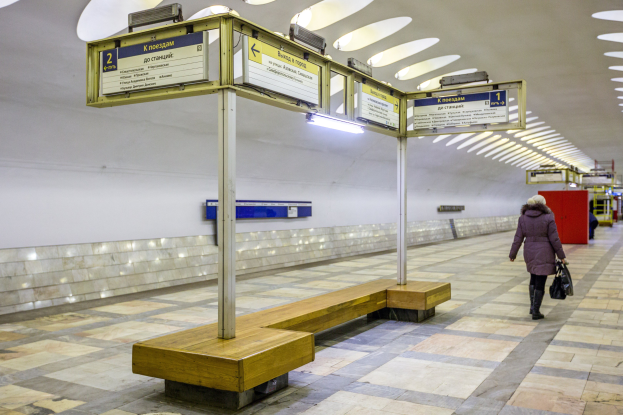 Eine Frau in einem Mantel mit einer Tasche geht durch eine Moskauer U-Bahn-Station mit Bänken, Informationsanzeigen und Beleuchtung.