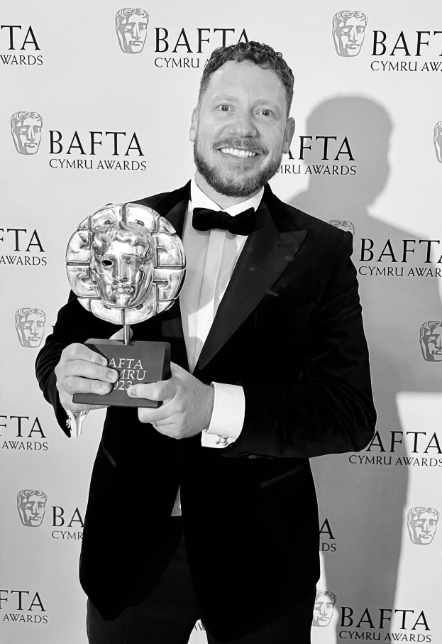 Ein Mann in einem Smoking, der eine BAFTA-Trophäe hält und lächelt, mit einer 'BAFTA Awards 2018'-Rückwand.
