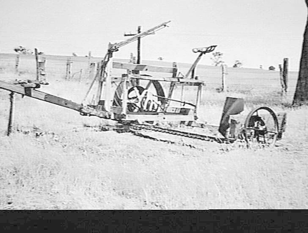 Schwarzes und weißes Foto eines alten Traktors in einem eingezäunten Feld mit Bäumen im Hintergrund.