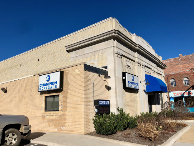 Gebäude mit "Champion Mortgage, Inc." -Schriftzug, geparktem Auto, Topfpflanzen, Bäumen und bewölktem Himmel.