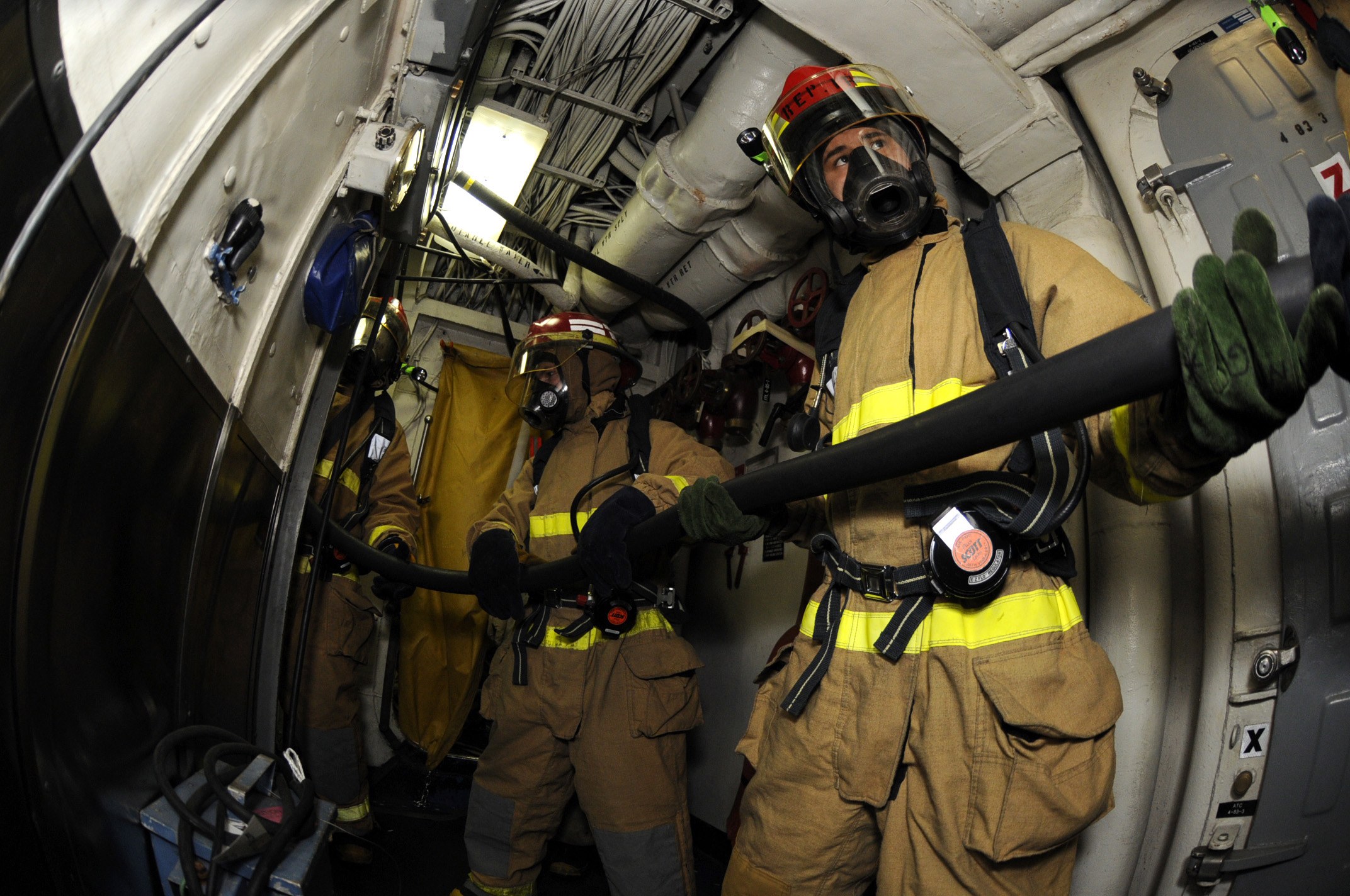 Feuerwehrleute mit Helmen und Handschuhen, die einen Schlauch in einem Flugzeug halten.