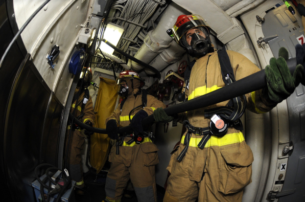Feuerwehrleute mit Helmen und Handschuhen, die einen Schlauch in einem Flugzeug halten.