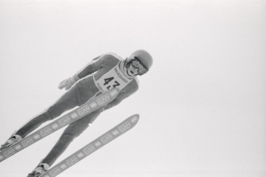 Skispringer in voller Ausrüstung springt in der Luft auf Skiern gegen einen klaren blauen Himmel