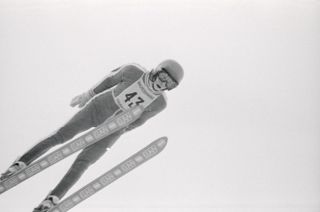 Skispringer in voller Ausrüstung springt in der Luft auf Skiern gegen einen klaren blauen Himmel