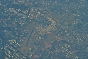 Eine Luftaufnahme eines Flughafens umgeben von Stadtgebäuden, Straßen und anderen Strukturen mit Text am unteren Bildrand.
