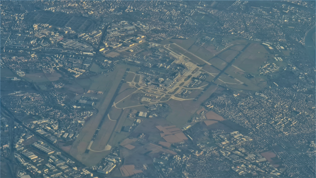 Eine Luftaufnahme eines Flughafens umgeben von Stadtgebäuden, Straßen und anderen Strukturen mit Text am unteren Bildrand.