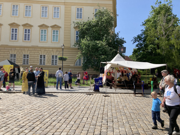 Eine Gruppe von Menschen geht eine Kopfsteinpflasterstraße in Krakaus altem Stadtzentrum während eines Festivals entlang, mit Zelten, Tischen mit Gegenständen und einem Gebäude mit sichtbarem Text im Hintergrund.