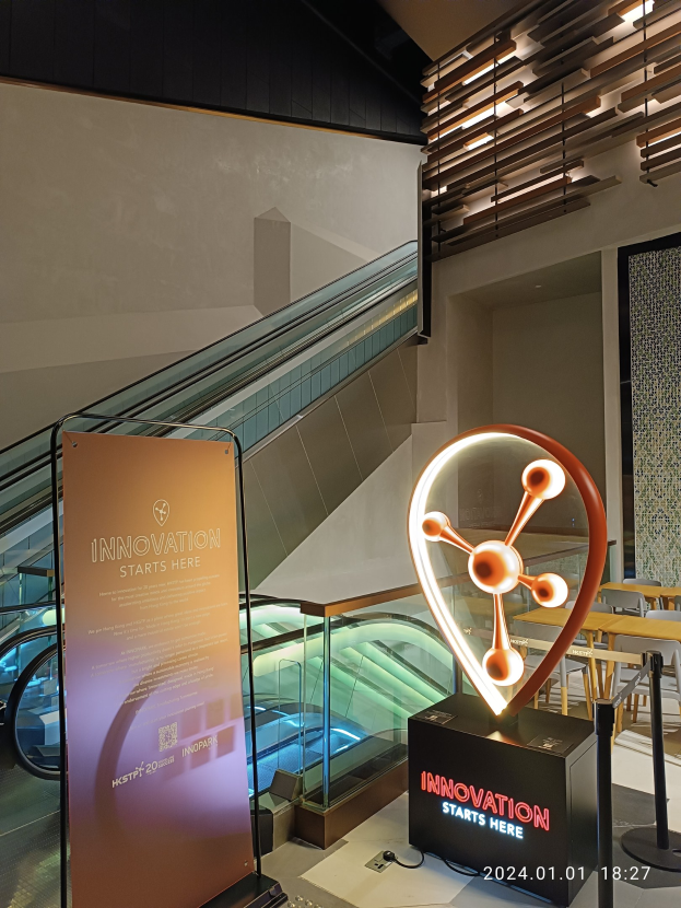 Großes Schild in der Mitte eines Gebäudes mit einer Rolltreppe im Hintergrund, flankiert von Tischen und Stühlen rechts und einer Tafel links, die 'Innovation Starts Here' anzeigt.