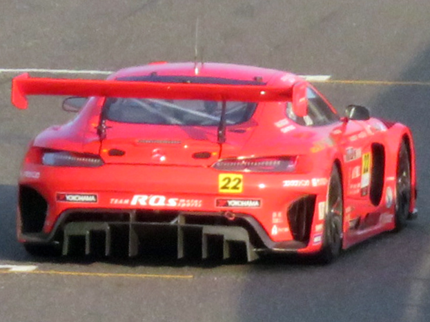 Roter Porsche 911 GTS Rennauto auf einer Rennstrecke mit aerodynamischem Design, großer Heckflügel und schwarzen Rädern.