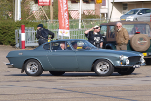 Eine Reihe von Autos mit Passagieren fährt auf einer Straße neben Gebäuden, Bäumen und verschiedenen städtischen Elementen, mit einer Straße unten.