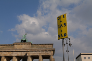 Das Brandenburg Tor in Berlin, Deutschland, mit einem gelben Schild, auf dem "Öl und Gas Krieg" steht, vor einem bewölkten Himmel.