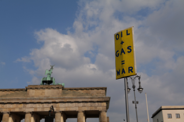 Das Brandenburg Tor in Berlin, Deutschland, mit einem gelben Schild, auf dem "Öl und Gas Krieg" steht, vor einem bewölkten Himmel.