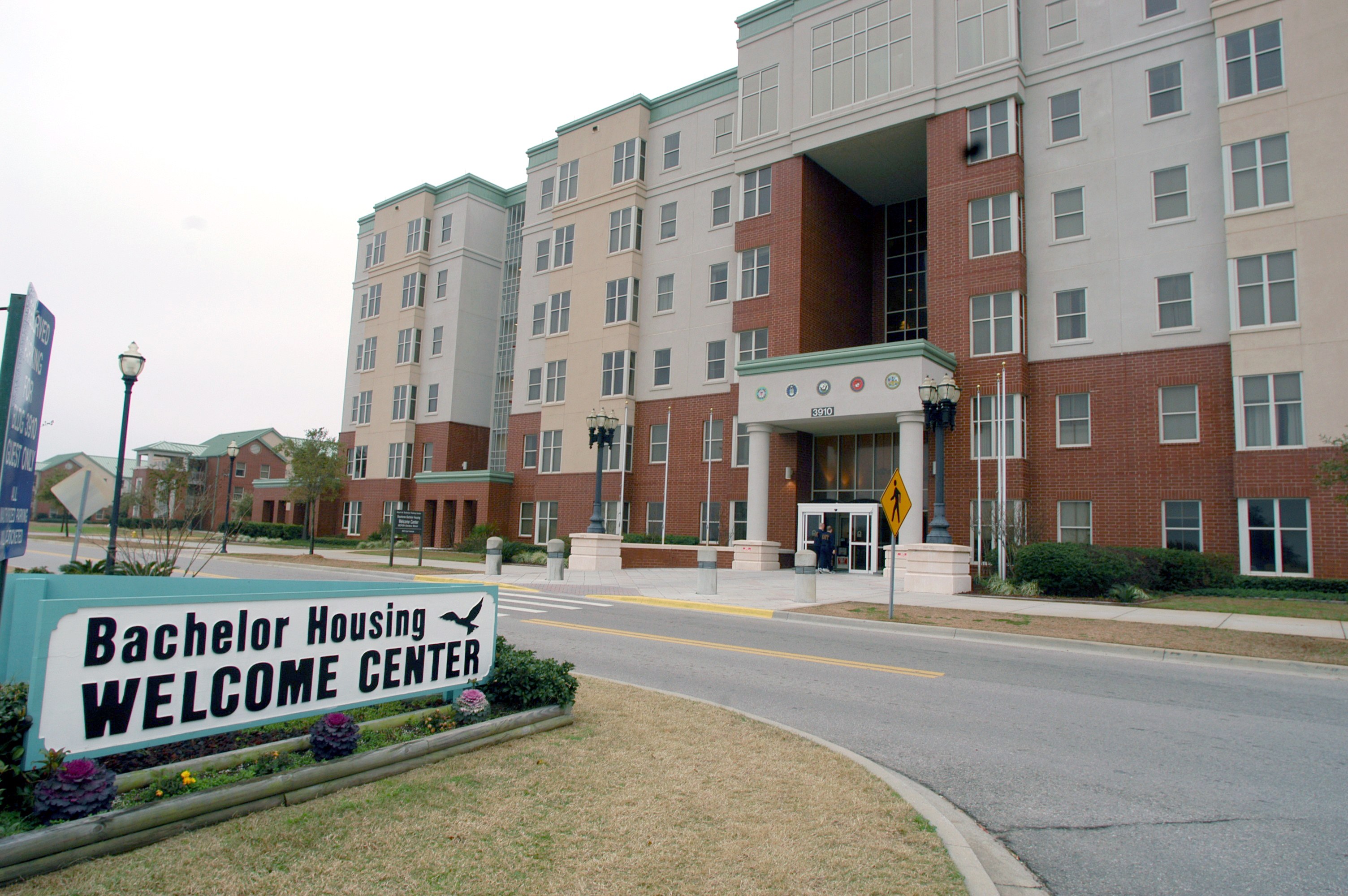 Ein Willkommenszentrum für Bachelor-Wohnheime mit Gebäuden, Straßenlaternen, Lampen, Schildern, Fahrzeugen, Grünflächen und einem klaren Himmel.
