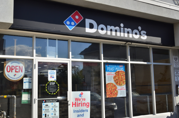 Außenansicht eines Domino's Pizza-Restaurants mit Glaswänden, die Stellenanzeigen und ein Namensschild an der Wand zeigen.