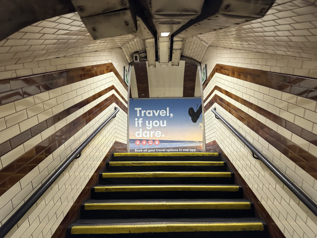 Eine Treppe in einer U-Bahn-Station mit einem "Reise, wenn du wagst"-Schild oben, flankiert von Geländern und Stationswänden im Hintergrund.