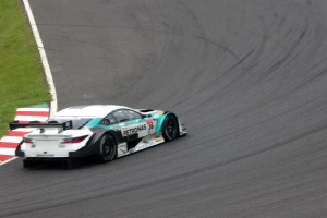 Ein silberner Mercedes-AMG GT3 Rennwagen auf einer Rennstrecke mit Text auf seinem Körper und Gras links.