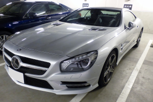 Silberner Mercedes-Benz SL-Class in einer Mehrgeschossigen Parkgarage neben anderen Fahrzeugen geparkt, mit Texttafeln und Betonwänden im Hintergrund sichtbar.