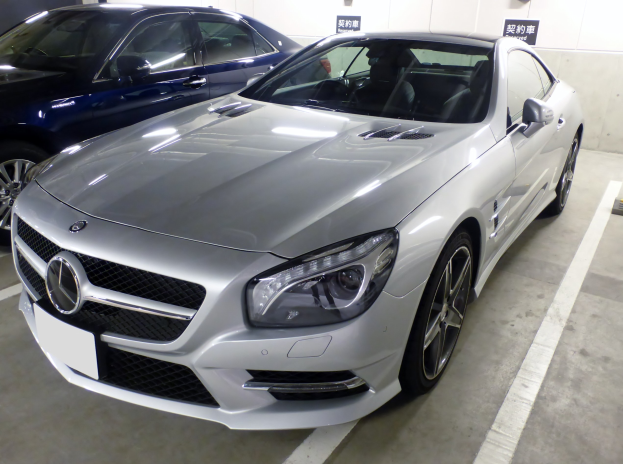 Silberner Mercedes-Benz SL-Class in einer Mehrgeschossigen Parkgarage neben anderen Fahrzeugen geparkt, mit Texttafeln und Betonwänden im Hintergrund sichtbar.