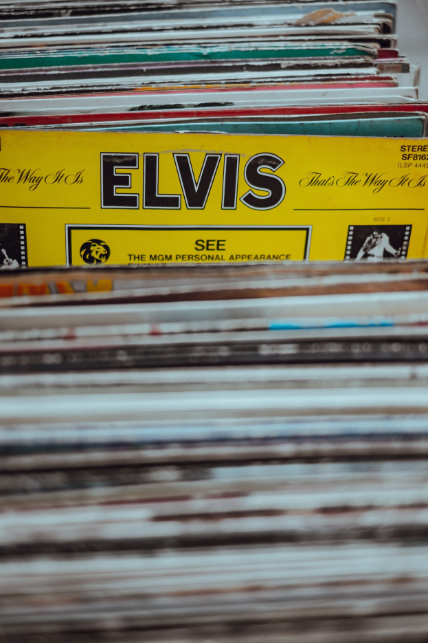Ein Stapel Elvis-Presley-Platten ordentlich auf einem Tisch gestapelt, mit einigen Platten, die sich überschneiden und Titel sichtbar sind, vor einem leicht unscharfen Hintergrund.