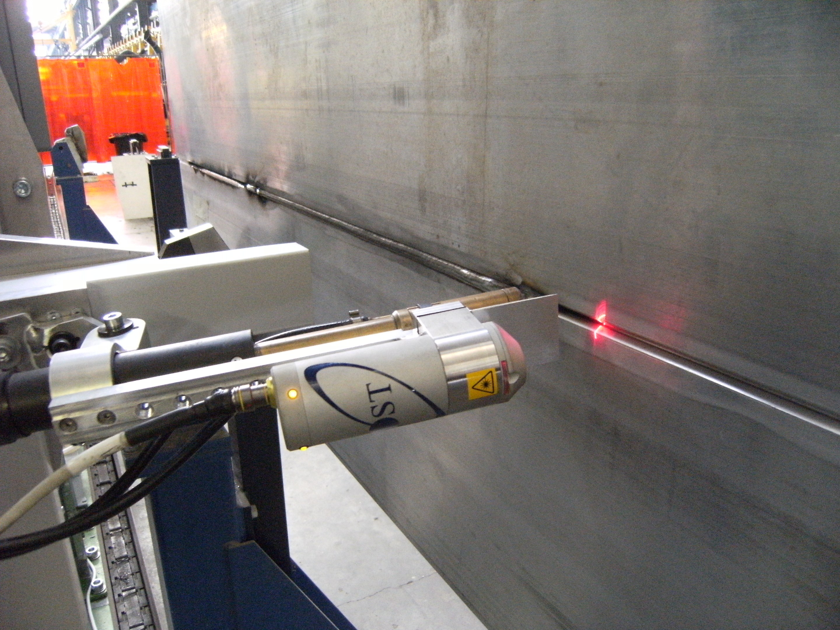 Eine Laserschneidmaschine in einer Fabrik, die helles Licht abstrahlt, mit einer Wand auf der rechten Seite und Gegenständen im Hintergrund.