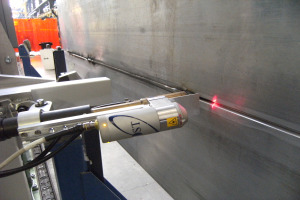 Eine Laserschneidmaschine in einer Fabrik, die helles Licht abstrahlt, mit einer Wand auf der rechten Seite und Gegenständen im Hintergrund.