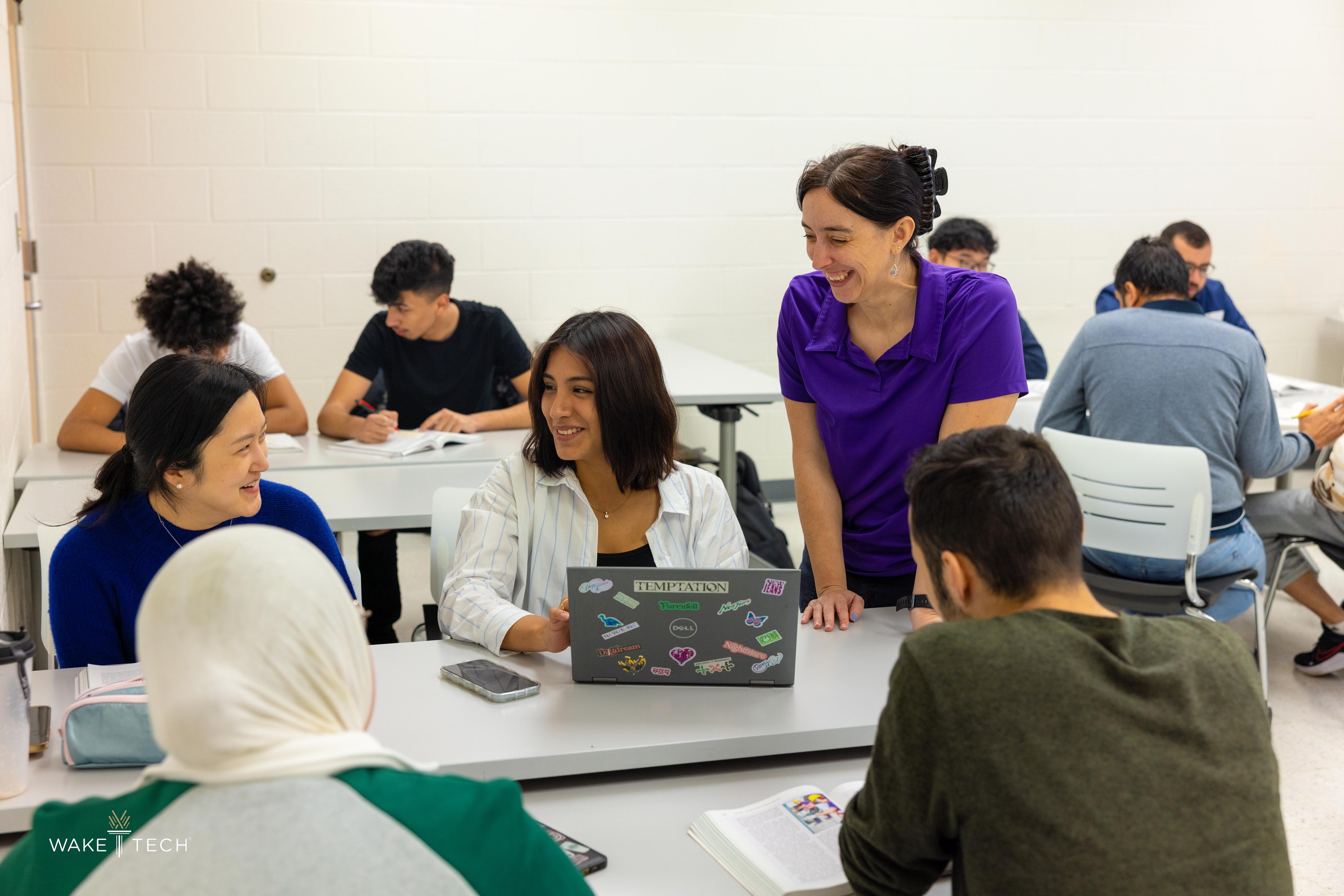 Eine Gruppe von Menschen in einem Klassenzimmer sitzt um einen Tisch mit Laptops, Büchern und anderen Gegenständen und diskutiert über Klimawandel, wie es der Titel "Wake Tech: Ein Leitfaden zum Klimawandel" angibt.