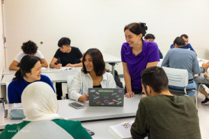Eine Gruppe von Menschen in einem Klassenzimmer sitzt um einen Tisch mit Laptops, Büchern und anderen Gegenständen und diskutiert über Klimawandel, wie es der Titel "Wake Tech: Ein Leitfaden zum Klimawandel" angibt.