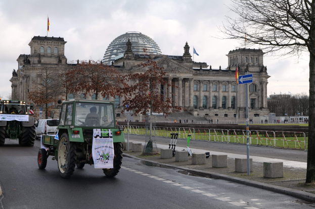 Traktorgruppe fährt vor dem Reichstagsgebäude in Berlin, Deutschland, vorbei, wobei die Fenster, Säulen und Flaggen des Gebäudes zu sehen sind.