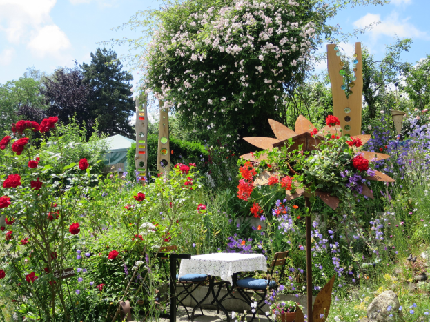 Ein Garten auf der Chelsea Flower Show mit bunten Blumen und Pflanzen, einem Tisch mit einer Decke in der Mitte und umgeben von Bäumen unter einem bewölkten Himmel.