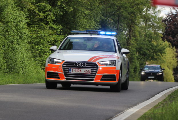 Audi A4 Polizeiwagen fährt auf einer grasbewachsenen Straße neben einem Wald, mit zwei Personen darin, unter einem klaren blauen Himmel.
