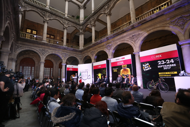 Eine Gruppe von Menschen sitzt an einem Tisch mit einem Podium und Mikrofon vor einer Menge, Kameras und Bannern während einer Pressekonferenz für das CDMX 2017-Event.