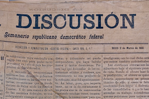 Ein gelblich-staubiges, leicht zerknittertes Zeitungsblatt mit der schwarzen Aufschrift "Diskussion", das die Schlagzeile "Semanario Repúblicano Democrático Federal" trägt.