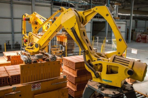Großes industrielles Lager mit gestapelten Kisten, Kranen, Zaun, Pfosten und einer fernen Wand in einer automatisierten Fertigungsumgebung.