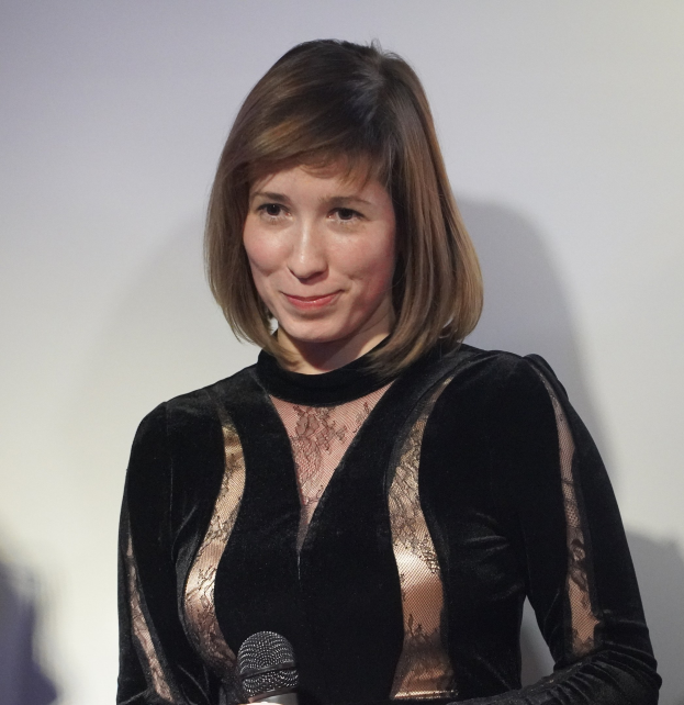 Frau in schwarzem Kleid mit Mikrofon während eines BBC Radio 1-Interviews, mit einer Wand im Hintergrund und einem selbstbewussten Gesichtsausdruck.