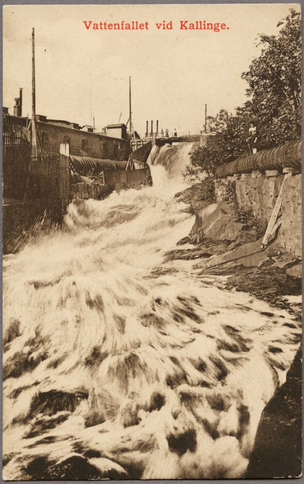 Altes Schwarz-Weiß-Foto eines Flusses mit fließendem Wasser, Bäumen, Gebäuden, Strommasten, einem Zaun und Text oben drauf.