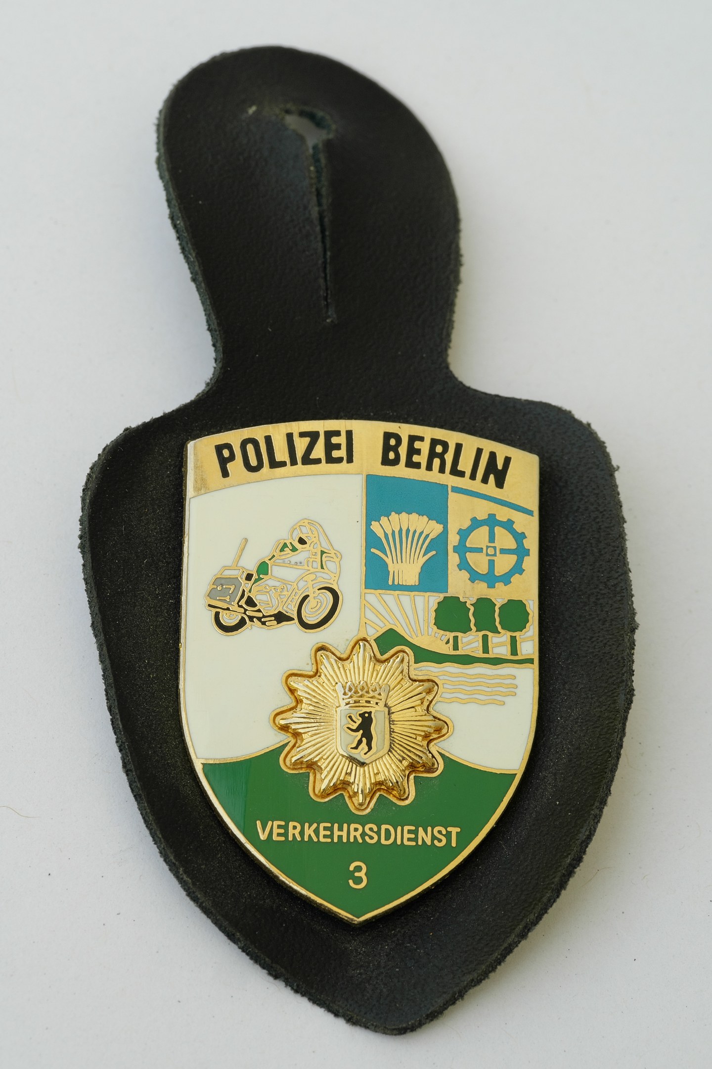 Ein schildförmiges Polizeibädge mit "Polizei Berlin" in schwarzer fetter Schrift auf einem blauen Hintergrund mit einem weißen Stern und Rand, auf einer Oberfläche plaziert.