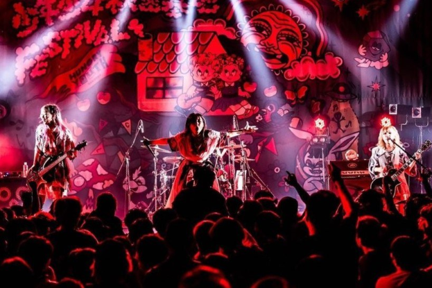Ein Live-Auftritt der japanischen Rockband Korn auf der Bühne mit Musikern, die Gitarren spielen und singen, begleitet von Mikrofonen und Ständern, während das Publikum unten zuschaut.