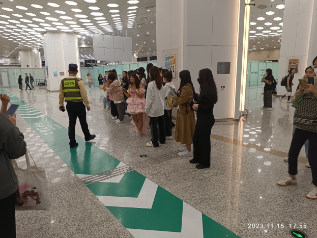 Menschen in der Schlange an einem Flughafen-Sicherheitscheck-in, mit Taschen und Mobiltelefonen, mit Säulen und Deckenleuchten im Hintergrund.