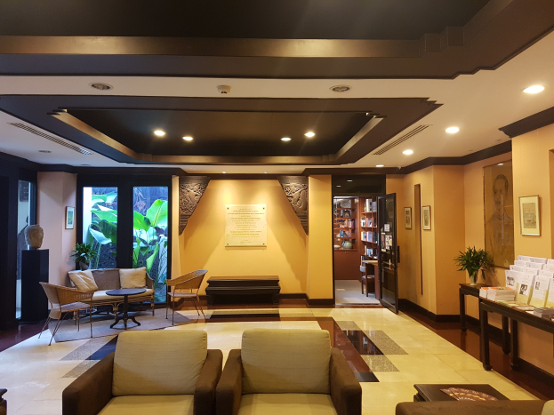 Ein Hotelfoyer mit Sofas, Stühlen, Tischen, Zimmerpflanzen, Büchern in Schränken, Deckenleuchten, Wandbehängen und Beistelltisch-Dekoration, gefüllt mit natürlichem Licht von Fenstern und Türen.