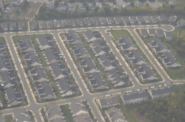 Luftbild eines Wohnviertels mit Häusern, Bäumen, Gras, Straßen und Fahrzeugen.